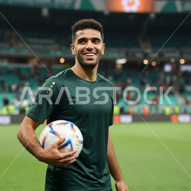 التحضير والتدريب و التجهز لبدء المباراة، مفهوم حب الرياضة، نمط الحياة الصحية، رياضات شبابية وأنشطة ترفيهية، لاعب عربي خليجي سعودي مبتسم يرتدي الزي الرياضي يحمل بيده كرة القدم بتعابير السرور والسعادة
