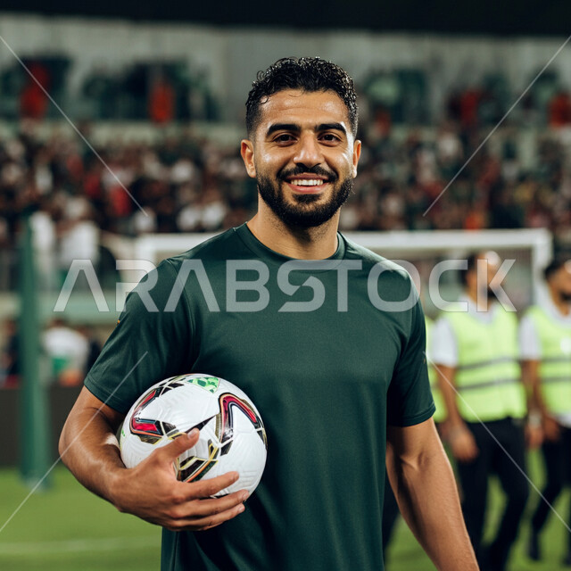 التحضير والتدريب و التجهز لبدء المباراة، مفهوم حب الرياضة، نمط الحياة الصحية، رياضات شبابية وأنشطة ترفيهية، لاعب عربي خليجي سعودي مبتسم يرتدي الزي الرياضي يحمل بيده كرة القدم بتعابير السرور والسعادة