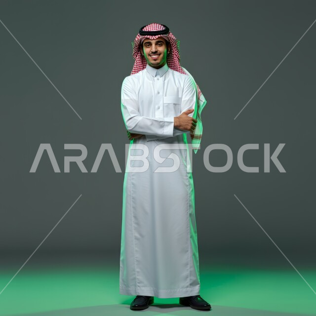 Looking at camera with crossed hands gestures, concept of elegance and masculinity, standing straight and confident, portrait of a handsome smiling young Saudi Arabian Gulf man wearing a traditional shemagh and thobe, interest in appearance, full body image, colorful background
