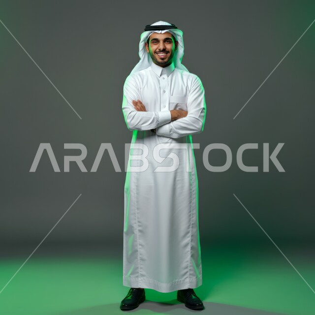 Concern about appearance, concept of elegance and masculinity, standing up straight and confident, portrait of a handsome happy young Saudi Arabian Gulf man wearing a white ghutra and traditional thobe looking at the camera with crossed hand gestures, full body image, colored background