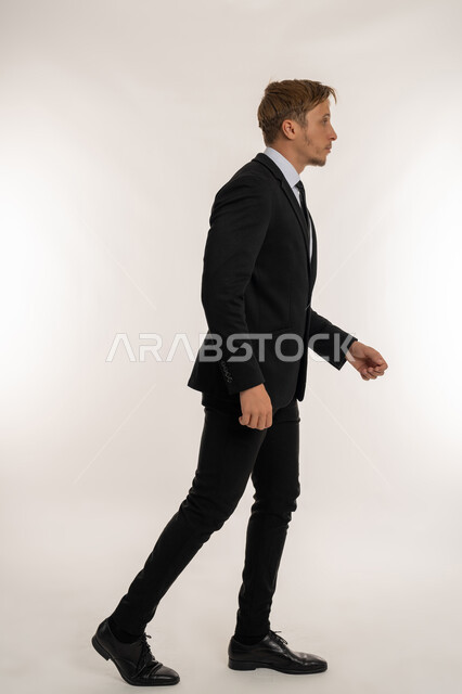 Gestures of walking and going to a certain place, the concept of elegance, masculinity and interest in external appearance, a side portrait of a foreign businessman wearing a formal suit walking forward with steady steps, looking at something with expressions of firmness and seriousness, a picture of the whole body, a white background