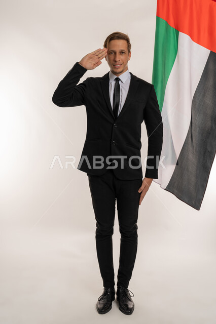 التعرف على ثقافات وتاريخ الامارات، بورتريه لرجل اعمال اجنبي مبتسم يرتدي البدلة الرسمية يرفع يده بتعابير القاء التحية، الاحتفال باليوم الوطني الامارتي2ديسمبر، النظر الى الكاميرا بتعابير الفخر والسرور، ذكرى تأسيس الاتحاد1971 ، صورة الجسم بالكامل، خلفية بيضاء