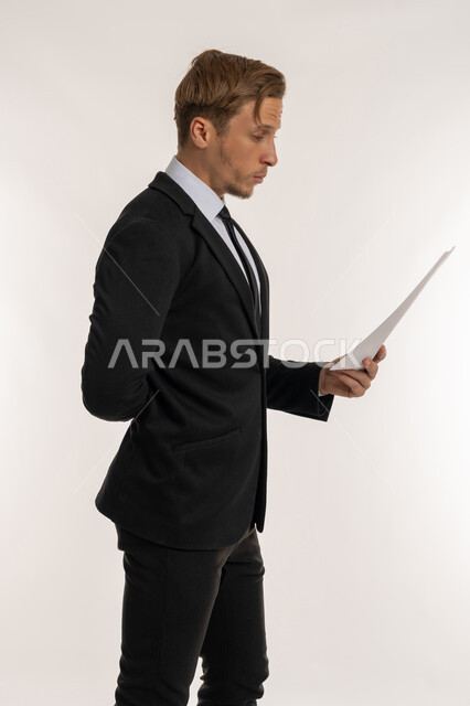 Expressions of thinking and concentration, careful reading of notes, preparing work reports, side portrait of a foreign businessman in a formal suit holding a set of documents and white papers, reviewing and following up on plans and projects with gestures of happiness and pleasure, white background