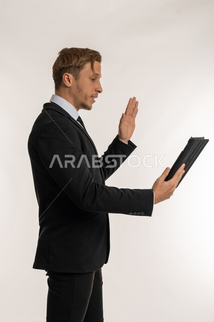 القاء التحية والترحيب والسلام، بورتريه من الجانب لرجل اعمال اجنبي يرتدي البدلة الرسمية يقوم بإجراء مكالمة فيديو باستخدام جهاز التابلت عبر الانترنت، التواصل مع العملاء والاهل والاصدقاء، دمج التقنية والتكنولوجيا في الحياة اليومية، عقد اجتماع عن بعد، خلفية بيضاء