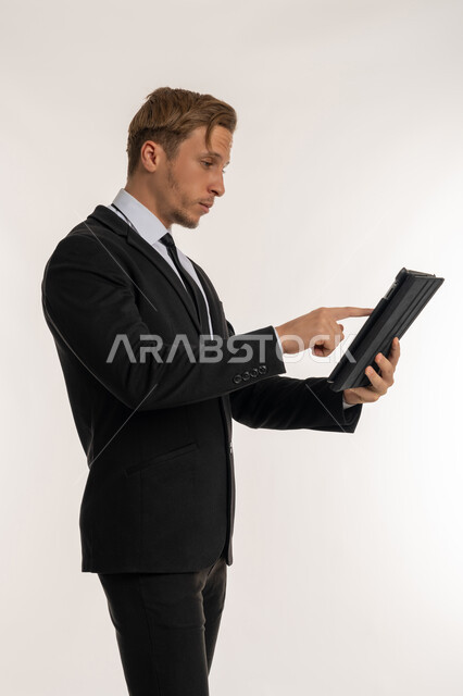 عقد اجتماع عمل، دمج الاجهزة الحديثة والتكنولوجيا في الحياة العملية، تصفح الانترنت وإنجاز المهام عن بعد، متابعه آخر أخبار السوشال ميديا، بورتريه من الجانب لرجل اعمال اجنبي يرتدي البدلة الرسمية يقوم باستخدام  جهاز التابلت, دردشة ومحادثات وتعارف, خلفية بيضاء