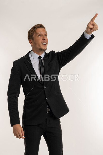 Determining a specific location with cheerful expressions, pointing with index finger to a specific target, indicating the location of an item, portrait of a smiling foreign man in a formal suit looking at something with gestures of happiness and pleasure, concept of elegance and masculinity, white background