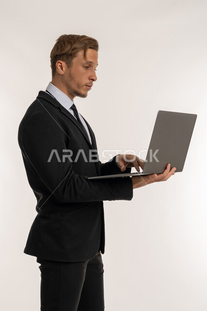 إدارة شؤون الأعمال وتنظيمها، استخدام التقنيات الحديثة المتطورة، عقد إجتماع عمل عبر الإنترنت، بورتريه من الجانب لرجل اعمال اجنبي يرتدي البدلة الرسمية يقوم بالعمل على الحاسب المحمول, دمج التكنولوجيا في الحياة العملية، خلفية بيضاء