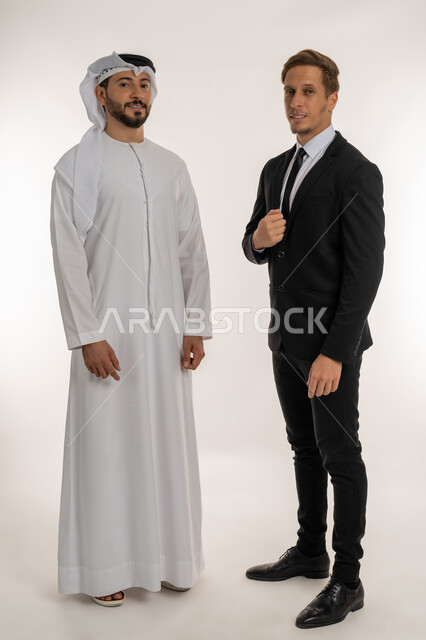 استضافة رجال الاعمال الأجانب في الامارات العربية المتحدة، تبادل الخبرات والمعرفة بين البلاد بورتريه لرجل عربي خليجي اماراتي يرتدي الكندورة والغترة يقف بجانب سائح اجنبي يرتدي البدلة الرسمية ينظران الى الكاميرا بتعابير السرور، صورة الجسم بالكامل، خلفية بيضاء