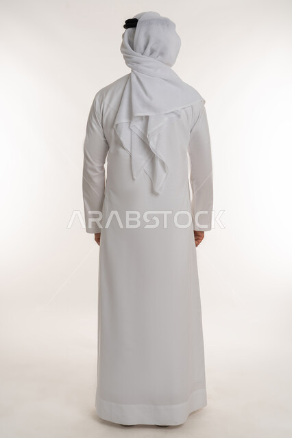 مفهوم الأناقة والرجولة والقوة, الاهتمام بالمظهر الخارجي، مفهوم الوقوف باستقامة وثقة، بورتريه من الخلف لرجل عربي خليجي إماراتي يرتدي الكندورة الاماراتية والغترة ينظر الى شيء ما، صورة لكامل الجسم، خلفية بيضاء