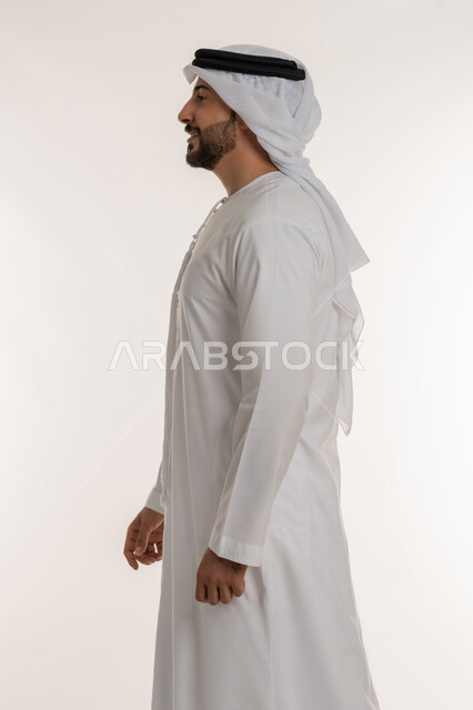 الاهتمام بالمظهر الخارجي، التقدم إلى الأمام بخطوات ثابتة، مفهوم الأناقة والرجولة والقوة, ايماءات المشي و الذهاب إلى مكان معين، بورتريه من الجانب لرجل عربي خليجي اماراتي يرتدي الكندورة والغترة ينظر إلى شيء ما بتعابير السرور والسعادة، خلفية بيضاء