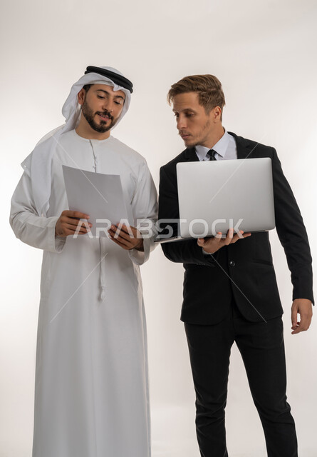 استضافة رجال الاعمال الاجانب في الامارات العربية المتحدة, تبادل الخبرات والمعرفة بين البلاد, بورتريه لرجل عربي خليجي اماراتي يرتدي الكندورة والغترة يقف بجانب شاب اجبني يرتدي البدلة الرسمية يقومان بالعمل على الحاسوب المحمول، خلفية بيضاء
