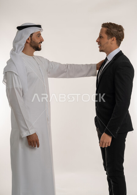 ايماءات البهجة والسعادة، تبادل الخبرات والمعرفة بين البلاد, استضافة رجال الاعمال الاجانب في الامارات العربية المتحدة, بورتريه لرجل عربي خليجي اماراتي يرتدي الكندورة والغترة يقف بجانب سائح اجبني يرتدي البدلة الرسمية يضع يده على كتفه بتعابير السرور, خلفية بيضاء