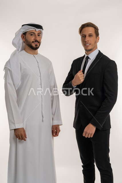 استضافة رجال الاعمال الاجانب في الامارات العربية المتحدة, تبادل الخبرات والمعرفة بين البلاد, بورتريه لرجل عربي خليجي اماراتي يرتدي الكندورة والغترة يقف بجانب سائح اجبني يرتدي البدلة الرسمية ينظران الى الكاميرا بتعابير السرور, خلفية بيضاء