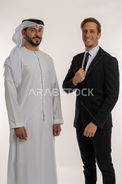 تبادل الخبرات والمعرفة بين البلاد, استضافة رجال الاعمال الاجانب في الامارات العربية المتحدة, بورتريه لرجل عربي خليجي اماراتي يرتدي الكندورة والغترة يقف بجانب سائح اجبني يرتدي البدلة الرسمية ينظران الى الكاميرا بتعابير السرور, خلفية بيضاء