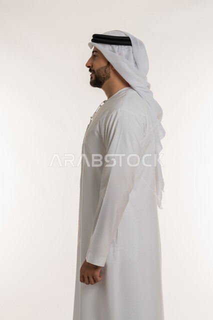 مفهوم الأناقة والرجولة والقوة, بورتريه من الجانب لرجل عربي خليجي إماراتي يرتدي الكندورة الاماراتية والغترة ينظر الى شيء ما, الوقوف باستقامة وثبات والنظر الى اليسار بايماءات الثقة بالنفس, تعابير الجدية والحزم، الاهتمام بالمظهر الخارجي، خلفية بيضاء