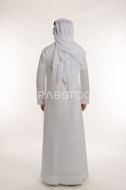Concept of masculinity and strength, elegance and interest in appearance, portrait from the back of a foreign man wearing an Emirati kandura and ghutra looking at something, standing straight and steady, objecting to a specific subject, full body length, white background