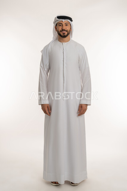 النظر الى الكاميرا بايماءات الثقة بالنفس, مفهوم الاناقة والرجولة, بورتريه لرجل عربي خليجي إماراتي مبتسم يرتدي الكندورة والغترة يقف باستقامة بتعابير البشاشة والسرور, الاهتمام بالمظهر الخارجي، الطول الكامل للجسم، خلفية بيضاء