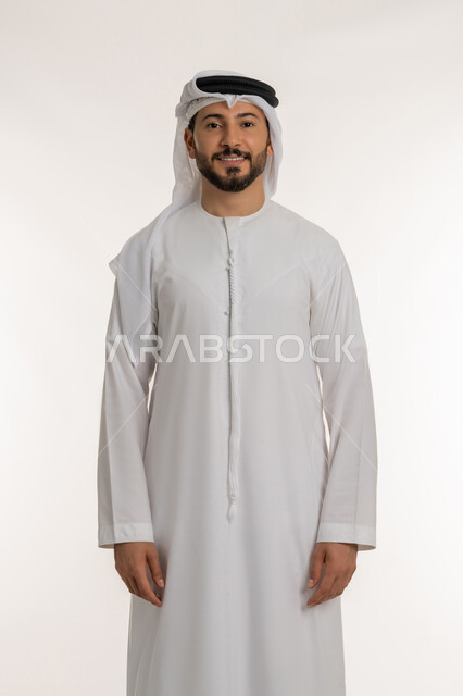 مفهوم الاناقة والرجولة, التقاط الصور الشخصية للوثائق الرسمية, بورتريه لرجل عربي خليجي إماراتي مبتسم يرتدي الكندورة والغترة يقف باستقامة بتعابير البشاشة والسرور, الاهتمام بالمظهر الخارجي، النظر الى الكاميرا بايماءات الثقة بالنفس, خلفية بيضاء