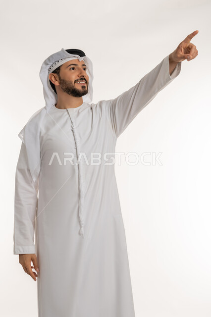 الاشارة بإصبع السبابة إلى هدف محدد, الدلالة على مكان عنصر, بورتريه لرجل عربي خليجي إماراتي مبتسم يرتدي الكندورة والغتره ينظر إلى شيء ما بإيماءات السعادة و السرور، تحديد موقع معين بتعابير البشاشة, خلفية بيضاء