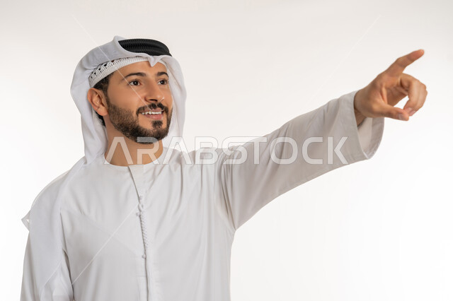 الدلالة على مكان عنصر, بورتريه مقرب لرجل عربي خليجي إماراتي مبتسم يرتدي الكندورة والغتره ينظر إلى شيء ما بإيماءات السعادة و السرور، تحديد موقع معين بتعابير البشاشة, الاشارة بإصبع السبابة إلى هدف محدد, خلفية بيضاء