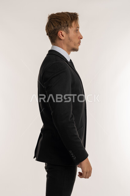 Concept of elegance, masculinity and strength, side portrait of a foreign man in a formal suit looking at something, standing straight and steady and looking to the right with gestures of self-confidence, expressions of seriousness and firmness, concern for appearance, white background