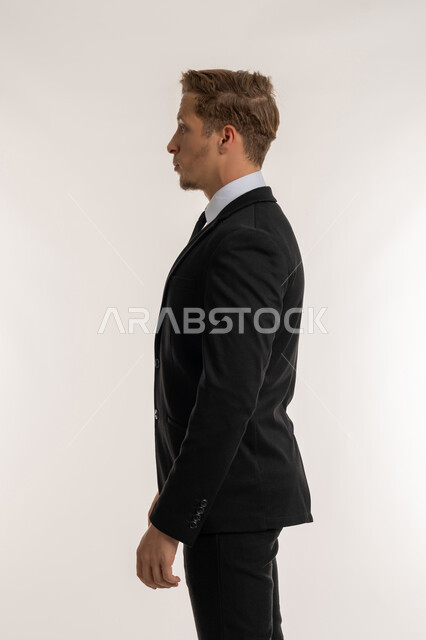 الوقوف باستقامة وثبات والنظر الى اليسار بايماءات الثقة بالنفس, تعابير الجدية والحزم، الاهتمام بالمظهر الخارجي، مفهوم الأناقة والرجولة والقوة, بورتريه من الجانب لرجل أعمال أجنبي يرتدي البدلة الرسمية ينظر الى شيء ما, خلفية بيضاء