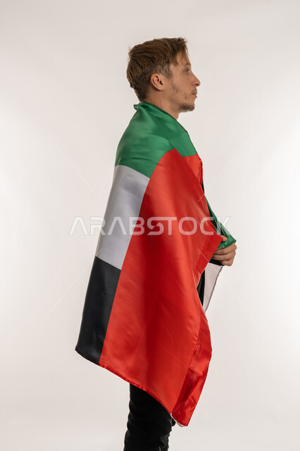 التعرف على ثقافات وتاريخ الامارات، بورتريه من الجانب لرجل اعمال اجنبي يرتدي البدلة الرسمية يحمل العلم على ظهره للاحتفال باليوم بالوطني الاماراتي 2 ديسمبر، الوقوف باستقامة وثبات بتعابير الفخر والسرور، ذكرى تأسيس الاتحاد 1971، خلفية بيضاء