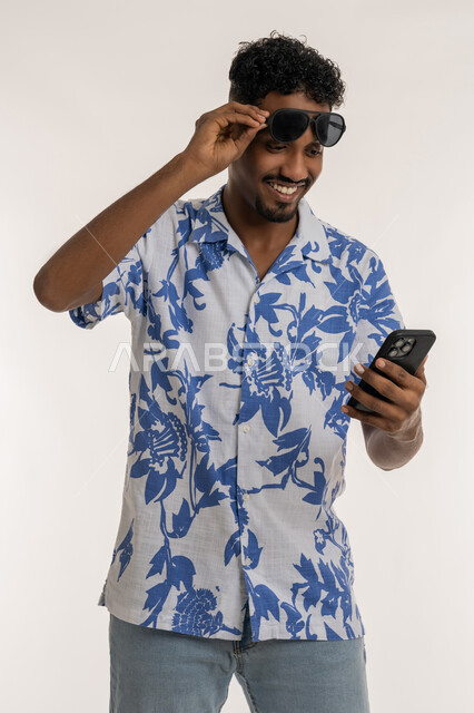رؤية الاخبار السعيدة، رجل سعودي يقوم باستخدام الاجهزة الحديثة، بورتريه لشاب اسمر عربي خليجي اماراتي مبتسم يرتدي الزي الكاجول يقوم برفع النظارات الشمسية عن عينه والنظر الى الهاتف بإيماءات السرور، متابعة اخر اخبار السوشال ميديا، خلفية بيضاء
