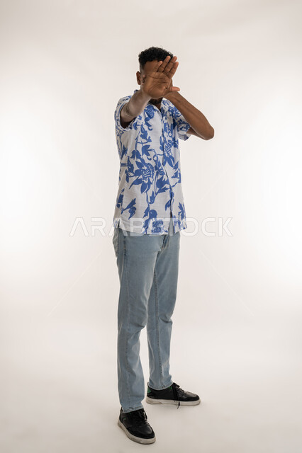 الاحساس بالانزعاج والرفض والفشل والخيبة، رجل سعودي يغمض عينيه لعدم الرؤية، بورتريه لشاب اسمر عربي خليجي اماراتي يرتدي الزي الكاجوال يرفع كفه للاعلى بايماءات عدم الاقتراب وطلب التوقف عن فعل أمر ما، الحزن والاحباط والرغبة بالبكاء، صورة الجسم بالكامل، خلفية بيضاء