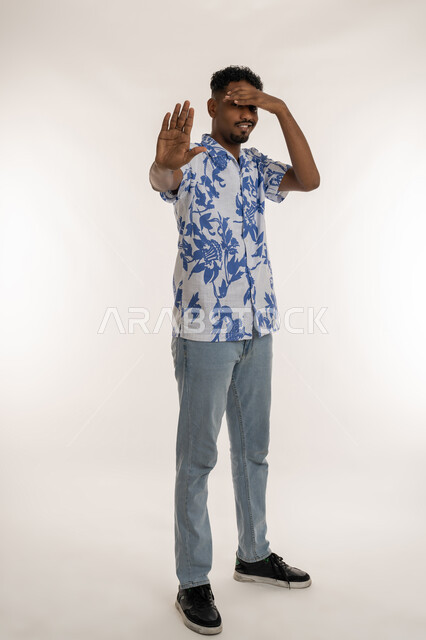 الإمتناع عن فعل شيء ما، رجل سعودي يرفع كفه للاعلى بتعابير طلب التوقف وعدم الاقتراب، بورتريه لشاب اسمر عربي خليجي اماراتي يرتدي الزي الكاجوال يضع يده على عينيه بإيماءات الخوف والذعر والصدمة، صورة الجسم بالكامل، خلفية بيضاء