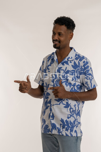الإشارة و التوضيح وتحديد موقع معين, رجل سعودي يقوم بالدلالة على مكان عنصر، بورتريه لشاب اسمر عربي خليجي اماراتي مبتسم يرتدي الزي الكاجوال يشير بإصبعيه السبابة لشيء ما بايماءات الفرد والتصويب، خلفية بيضاء