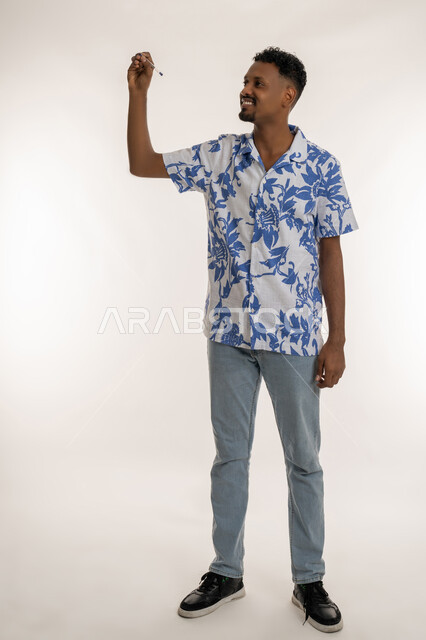 الاستعداد لتدوين وتحديد شيء ما، بورتريه لرجل اسمر عربي خليجي إماراتي يرتدي الزي الكاجوال يمسك بيده قلم يرفع يده بايماءات الكتابة، رجل سعودي يقوم بالرسم والتخطيط والإشارة على الهواء، صورة لكامل الجسم، خلفية بيضاء