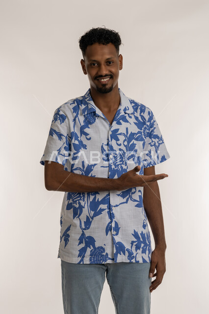 Locating a specific thing, hand gestures indicating this place "here", a Saudi man pointing his hand to the left, a portrait of an Arab Gulf Emirati man wearing casual clothes pointing his hand to the left looking at the camera with cheerful gestures, the concept of elegance and interest in external appearance, white background