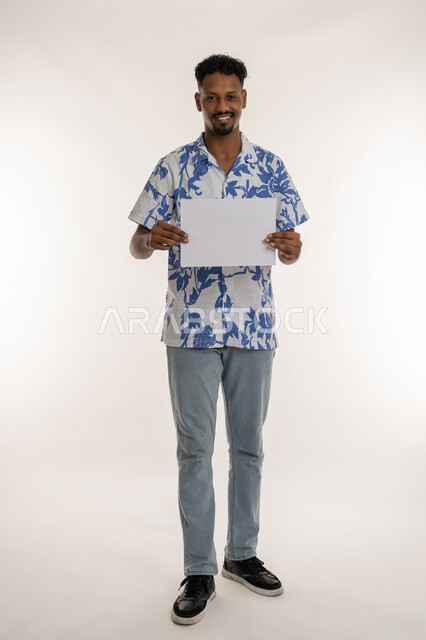 موك اب أبيض مستطيل، مفهوم الإعلان والتسويق، بورتريه لرجل عربي خليجي اماراتي مبتسم يرتدي الزي الكاجوال يحمل بيده لوحه بيضاء، شاب سعودي يمسك لافتة إعلانية فارغة ،استخدام لوحات توضيحية، صورة لكامل الجسم، خلفية بيضاء