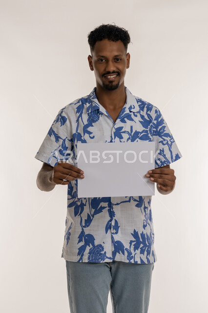 مفهوم الاعلان والتسويق، موك اب أبيض مستطيل، بورتريه لرجل عربي خليجي اماراتي مبتسم يرتدي الزي الكاجوال يحمل بيده لوحه بيضاء، شاب سعودي يمسك لافتة إعلانية فارغة ،استخدام لوحات توضيحية، خلفية بيضاء