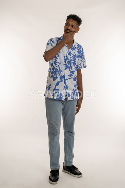 Planning for the future and setting future goals, looking away absentmindedly, portrait of a young dark-skinned Arab Gulf Emirati man wearing casual clothes, putting his hand on his chin with anxious gestures, man thinking about something, full body photo, white background