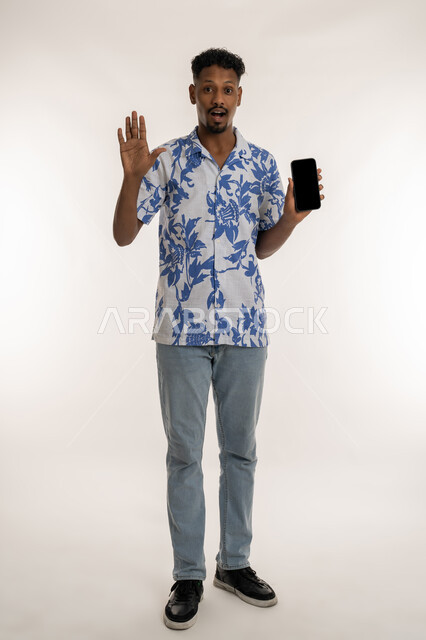 النظر الى الكاميرا بتعابير الدهشة والذهول، الاستفادة من خدمات وتطبيقات الجوال، دمج التكنولوجيا والاجهزة الحديثة في الحياة اليومية، بورتريه لرجل عربي خليجي اماراتي مبتسم يرتدي الزي لكاجوال يقوم بعرض شاشة سوداء فارغة، رجل سعودي يحمل بيده الهاتف المحمول، صورة لكامل الجسم، خلفية بيضاء