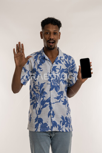 الاستفادة من خدمات وتطبيقات الجوال، النظر الى الكاميرا بتعابير الدهشة والذهول، دمج التكنولوجيا والاجهزة الحديثة في الحياة اليومية، بورتريه لرجل عربي خليجي اماراتي مبتسم يرتدي الزي لكاجوال يقوم بعرض شاشة سوداء فارغة، رجل سعودي يحمل بيده الهاتف المحمول، خلفية بيضاء