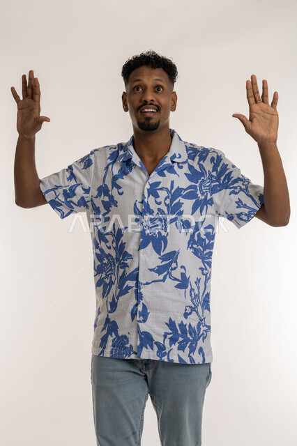 الشعور بالدهشة والصدمة والذهول, رجل سعودي ينظرلمكان ما تعابير التفاجؤ من سماع خبر ما، بورتريه لشاب اسمر عربي خليجي اماراتي يرتدي الزي الكاجوال يرفع يديه الى الاعلى بإيماءات الخوف والذعر, خلفية بيضاء