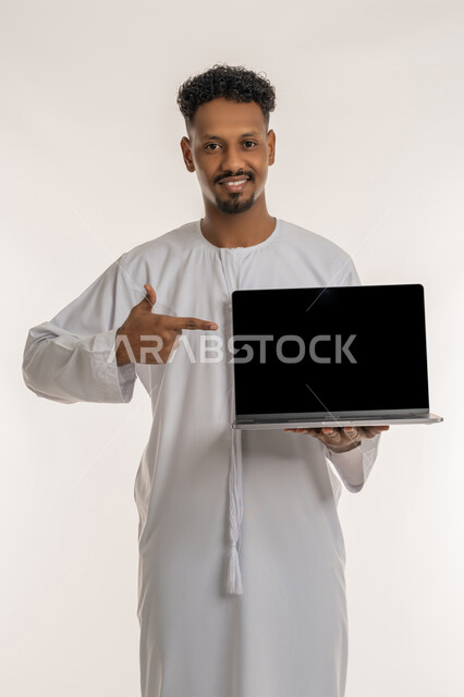 عرض صفحات الويب والبرامج والتطبيقات الالكترونية، بورتريه لرجل عربي خليجي إماراتي يرتدي الكندورة الإماراتية يحمل حاسوب محمول بشاشة سوداء فارغة يشير باصبع السبابة نحوه، استخدام الاجهزة والتقنيات الحديثة، خلفية بيضاء
