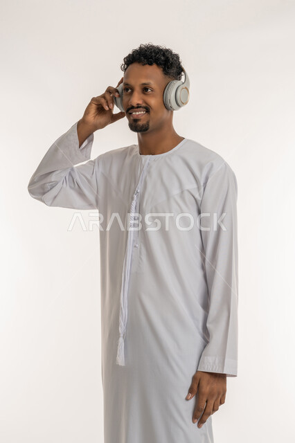 مواهب غنائية فنية, مفهوم الإستماع و الإصغاء بإستخدام الهيدفون، بورتريه لشاب عربي خليجي إماراتي يرتدي الكندورة الإماراتية ويضع سماعة الرأس بإيماءات السعادة والطرب، قضاء أوقات ممتعة بالإستماع إلى الأغاني، خلفية بيضاء