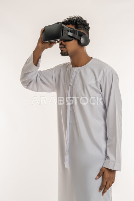 التطور التقني والتكنولوجي, بورتريه  لشاب عربي خليجي إماراتي يرتدي الكندورة ينظر من خلال نظارات ثلاثية الأبعاد (الفي ار), الاندماج ومحاكاة العالم الخيالي، تعابير الاندهاش والتفاجؤ، المتعة و التسلية بالمشاهدة عبر نظارة الواقع الافتراضي، خلفية بيضاء