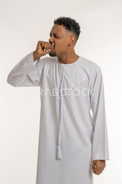 Feeling sick and coughing, need to see a doctor and receive treatment, infection with the Corona virus, influenza and pneumonia, portrait of a young Arab Gulf Emirati man wearing a white Emirati kandura suffering from a severe cough, white background