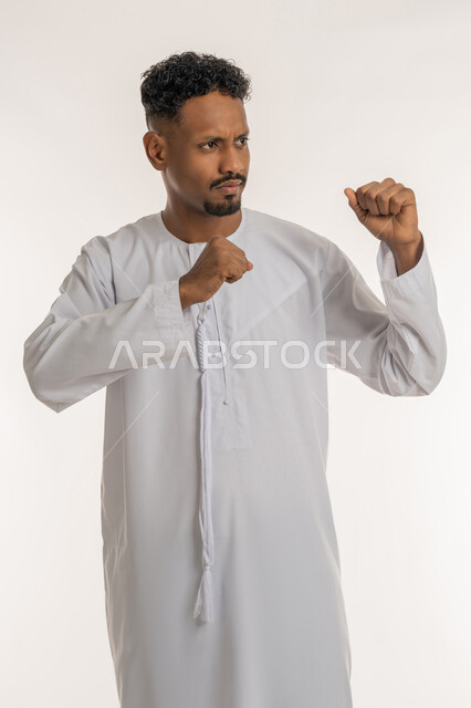 إتقان فنون الملاكمة، زيادة قدرة العضلات على التحمل، بورتريه لشاب عربي خليجي إماراتي يرتدي الكندورة الإماراتية يرفع قبضات يديه لتصدي الضربة، ممارسة رياضة الدفاع عن النفس، إيماءات القوة والتحدي، خلفية بيضاء