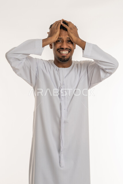 الشعور بالدهشة والذهول, تذكر شيء ما، بورتريه لشاب عربي خليجي إماراتي يرتدي الكندورة الإماراتية يضع يديه على رأسه بإيماءات التعجب والانبهار, النظر إلى الكاميرا بايماءات الصدمة, التفاجؤ من موقف محدد، خلفية بيضاء