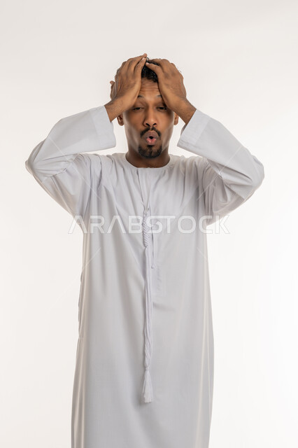 التفاجؤ من موقف محدد، الشعور بالدهشة والذهول, تذكر شيء ما، بورتريه لشاب عربي خليجي إماراتي يرتدي الكندورة الإماراتية يضع يديه على رأسه بإيماءات التعجب والانبهار, النظر إلى الكاميرا بايماءات الصدمة, خلفية بيضاء