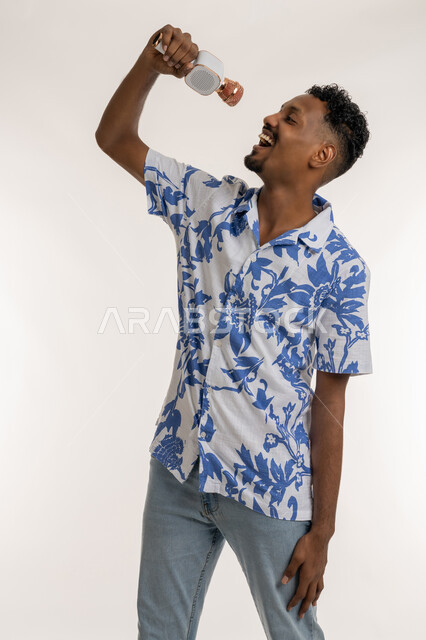 العمل في تقديم الفقرات والبرامج الفنية الترفيهية، قضاء وقت ممتع بأداء العروض الصوتية، بورتريه لرجل عربي اماراتي خليجي يرتدي الزي الكاجوال يمسك بيده المايك  ويغني بحماس، شاب سعودي بايماءات السعادة والاندماج والتفاعل مع الغناء، تسجيل مقطع صوتي غنائي، خلفية بيضاء