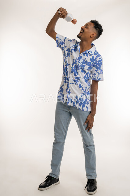 Gestures of happiness and integration with singing, presenting entertainment segments and programs, having a good time performing vocal performances, portrait of an Emirati Gulf Arab man wearing casual clothes holding a microphone in his hand and singing enthusiastically, a Saudi young man recording a singing audio clip, full body length, white background