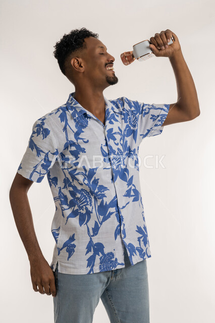 تسجيل مقطع صوتي غنائي، تقديم الفقرات والبرامج الفنية الترفيهية، قضاء وقت ممتع بأداء العروض الصوتية، بورتريه لرجل عربي اماراتي خليجي يرتدي الزي الكاجوال يمسك بيده المايك ويغني بحماس، شاب سعودي بايماءات السعادة والاندماج والتفاعل مع الغناء، خلفية بيضاء