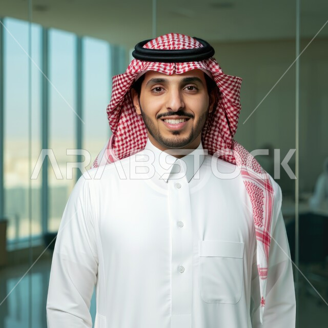 التوظيف في القطاع الإداري والمكتبي، مهن ووظائف للشباب في السعودية، العمل في المكاتب المطلة على الأبراج وناطحات السحاب الشاهقة في المدينة، صورة مقربة لشاب عربي خليجي سعودي يرتدي الثوب التقليدي والشماغ ينظر إلى الكاميرا بإيماءات السعادة والسرور